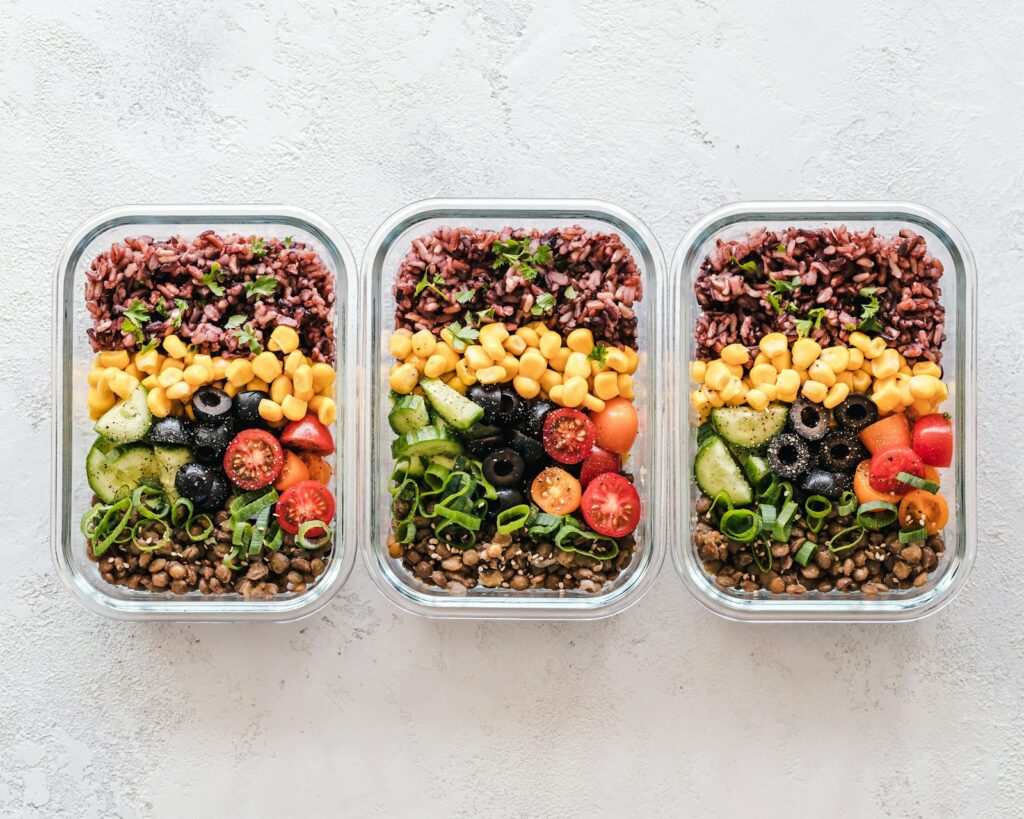 Trois contenants en verre remplis de riz, de maïs, d’olives, de tomates, de concombres et de lentilles