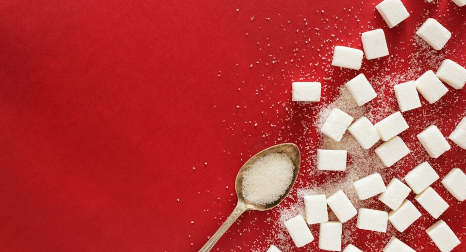 des morceaux de sucre et une cuillère sur une surface rouge