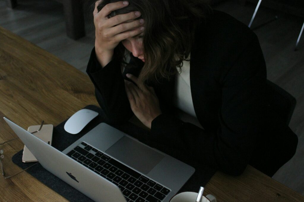 Femme stressée, la tête dans les mains devant l’ordinateur portable