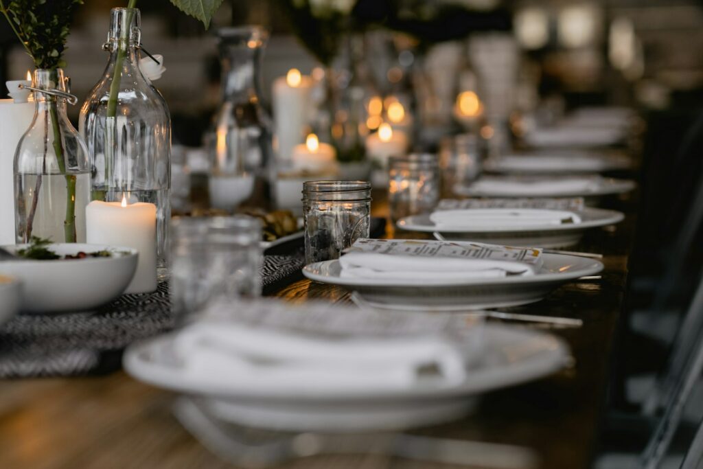 Une longue table à manger dressée avec des assiettes blanches, des bougies et des bouteilles en verre