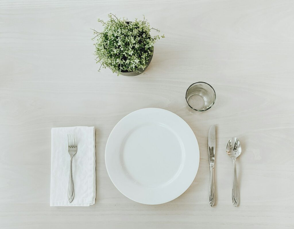 Assiette en céramique blanche à côté d’une fourchette en acier inoxydable et d’un couteau à pain sur une table blanche