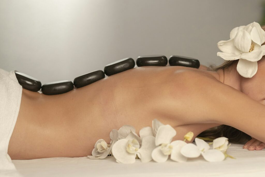 Une personne allongée sur une table de massage avec des pierres noires lisses dans le dos